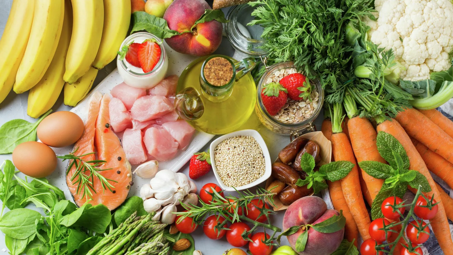 Набор полезных продуктов для сбалансированного питания: овощи, фрукты, рыба, яйца, крупы, йогурт, оливковое масло и зелень на столе