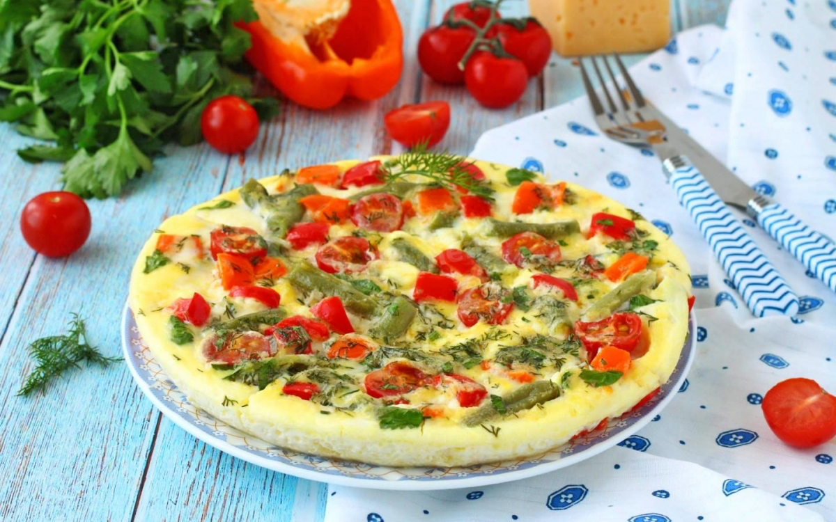 Омлет с овощами, зеленью и помидорами на тарелке, рядом свежие овощи и зелень