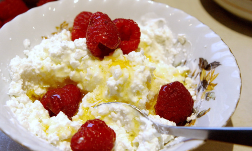 Творог с малиной и мёдом в тарелке, ложка внутри